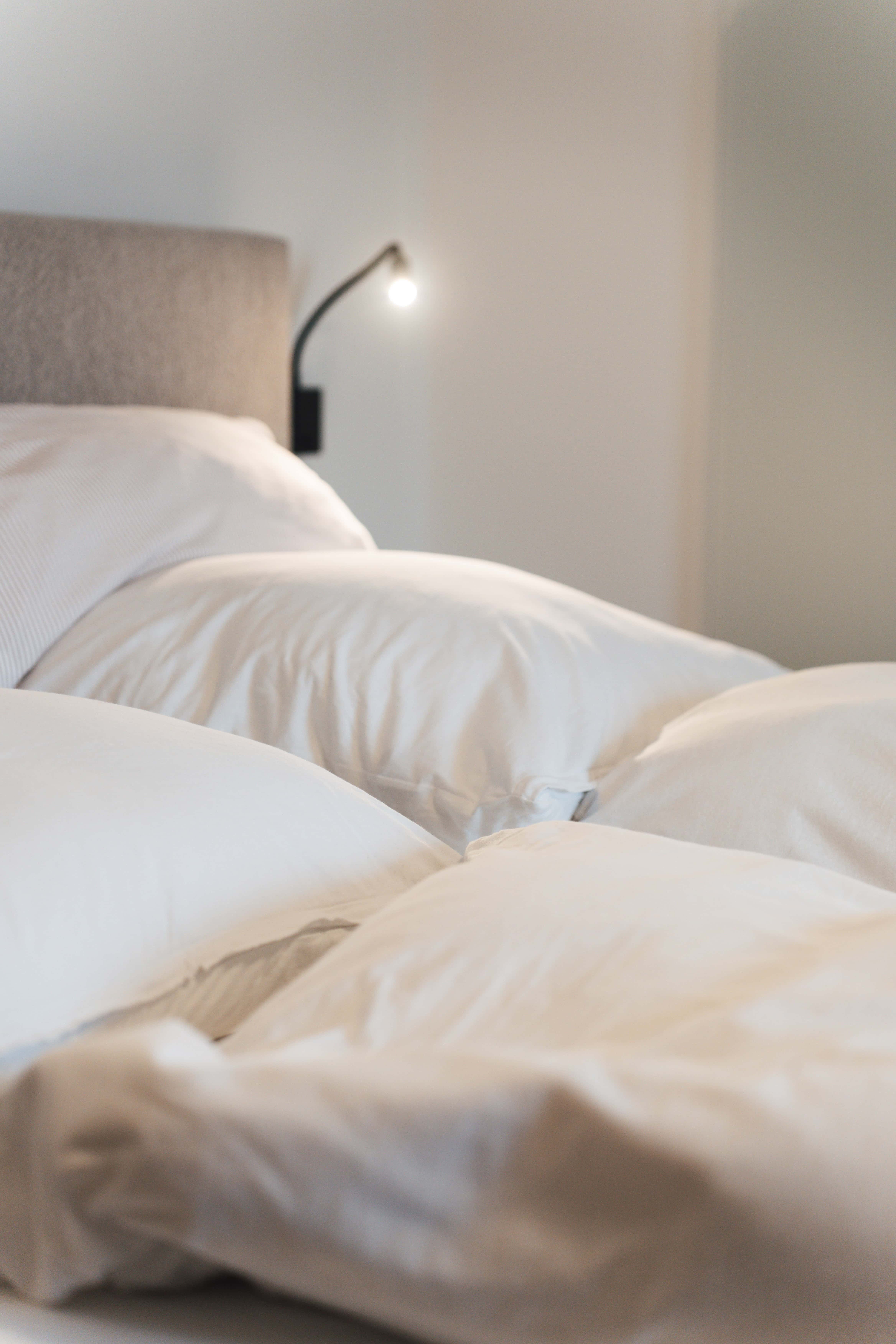 Komfortables Schlafzimmer mit weißen Bettwäsche und Leselampe an der Wand.