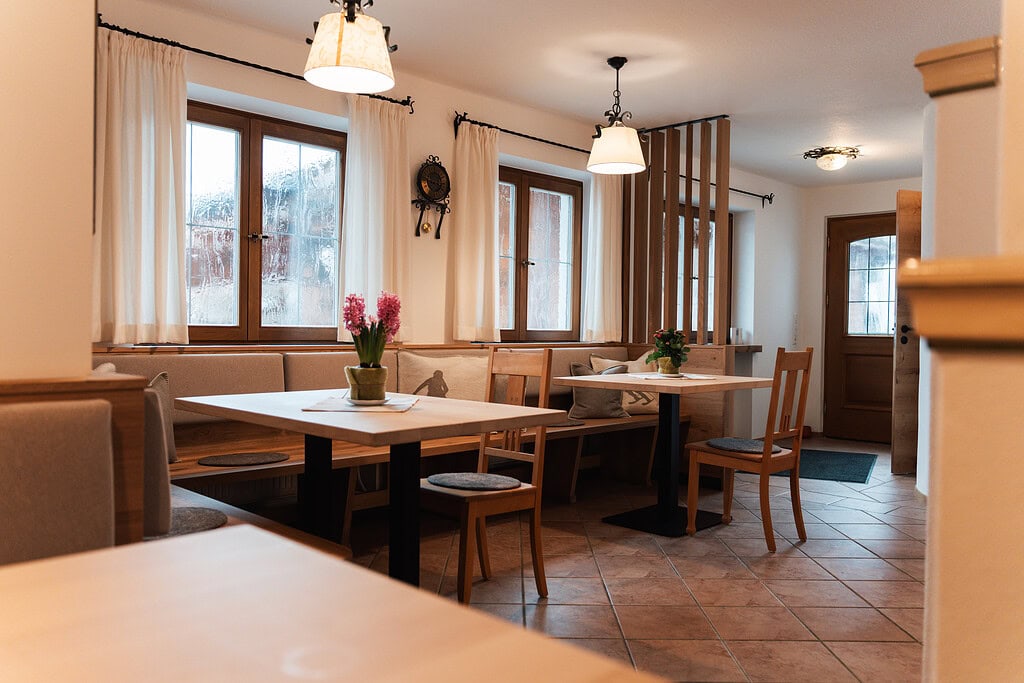Gem&uuml;tlicher Speiseraum mit Holzm&ouml;beln und gro&szlig;en Fenstern im G&auml;stehaus Reit im Winkl.