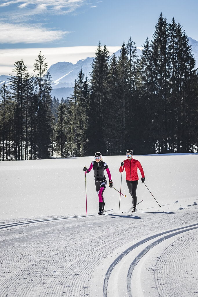 Zwei Personen beim Schneeschuhwandern in verschneiter Winterlandschaft, umgeben von Tannenbäumen und.